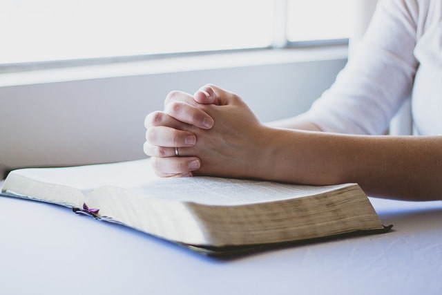 Hand in prayer on Bible